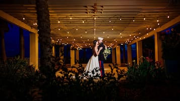 Una pareja se abraza bajo una pérgola iluminada con luces al anochecer.
