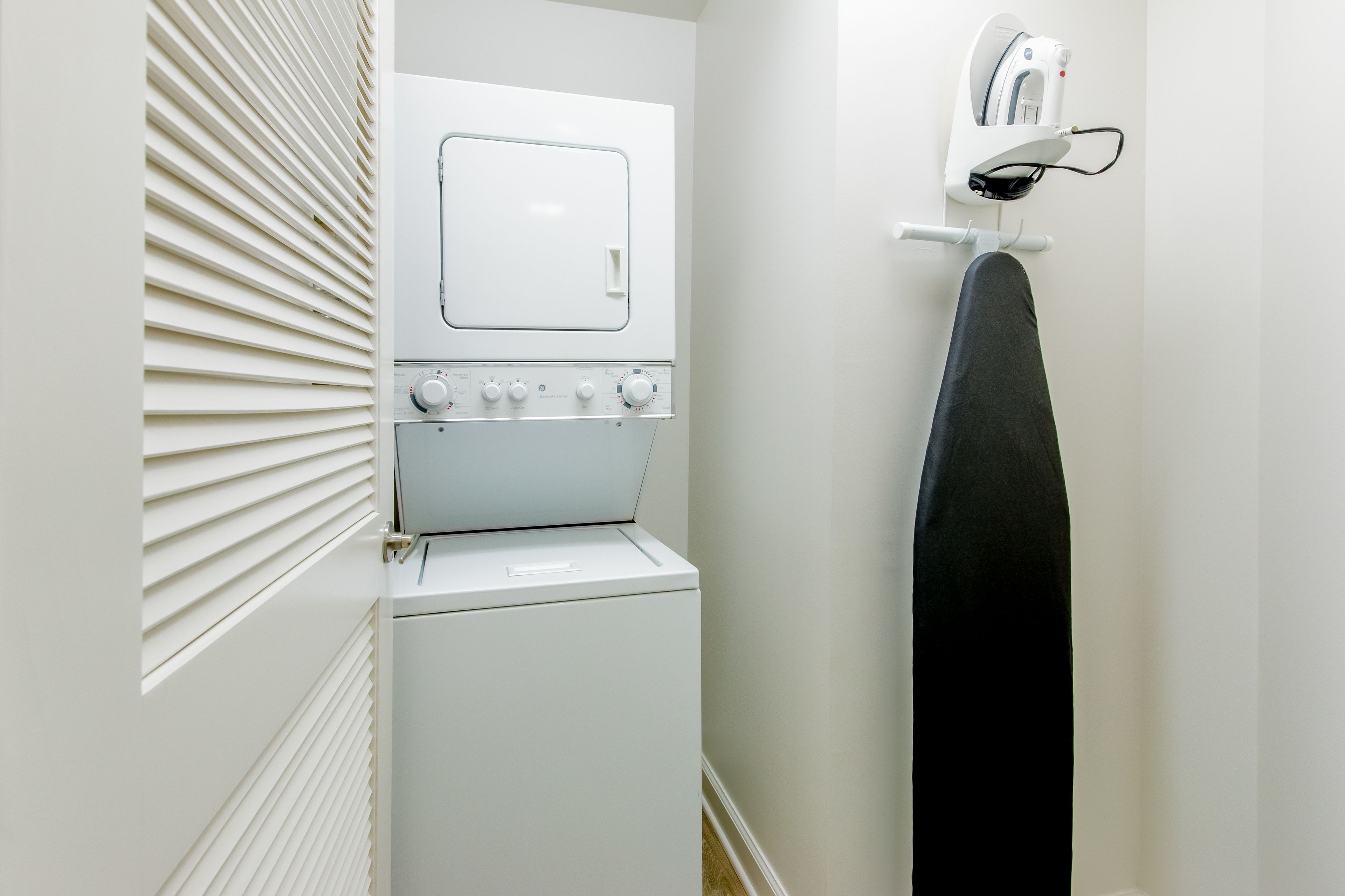 A compact laundry area with a washing machine, dryer, and ironing station.