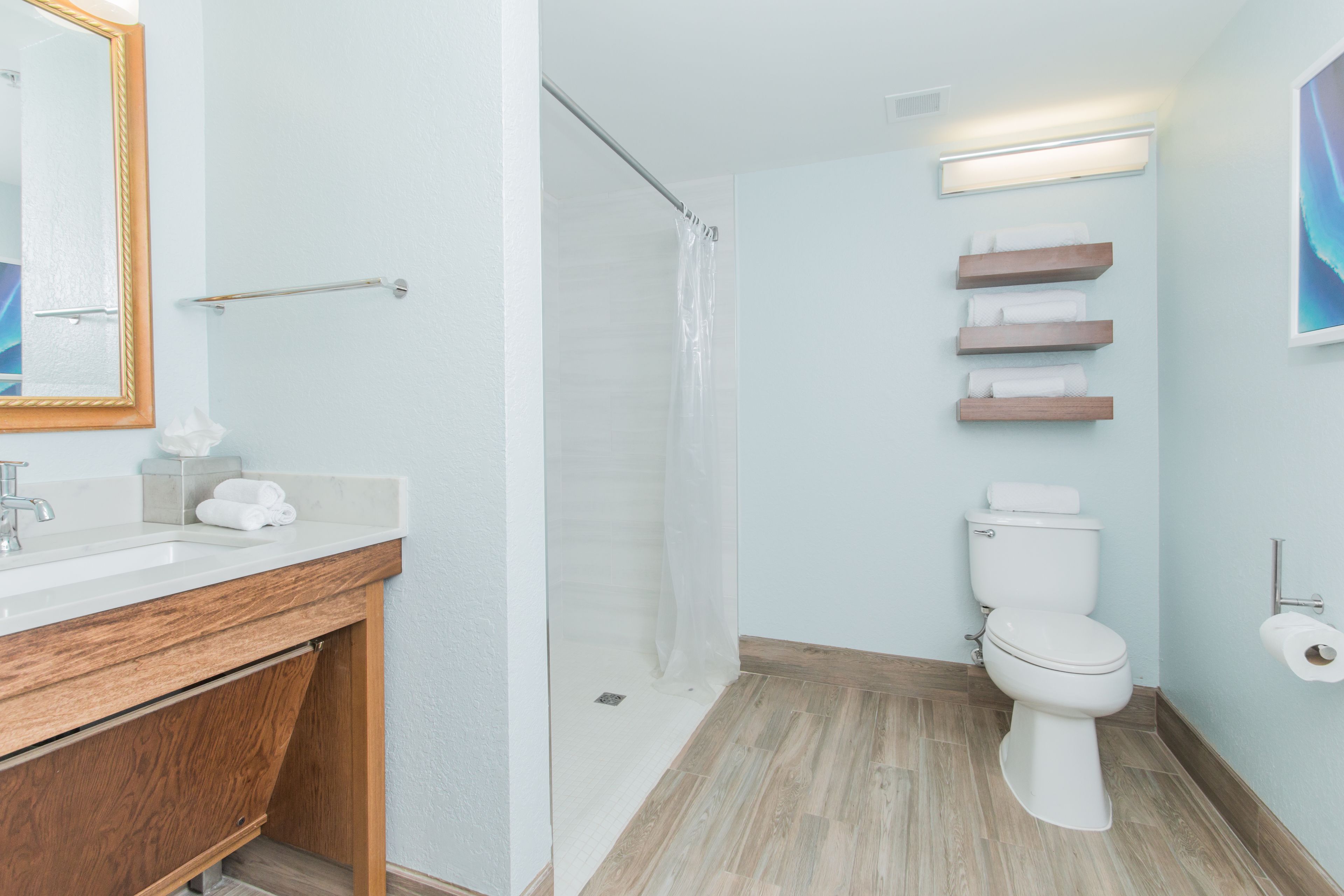 A modern bathroom with a wooden vanity, a glass shower enclosure, and a toilet with built-in shelves for towels.