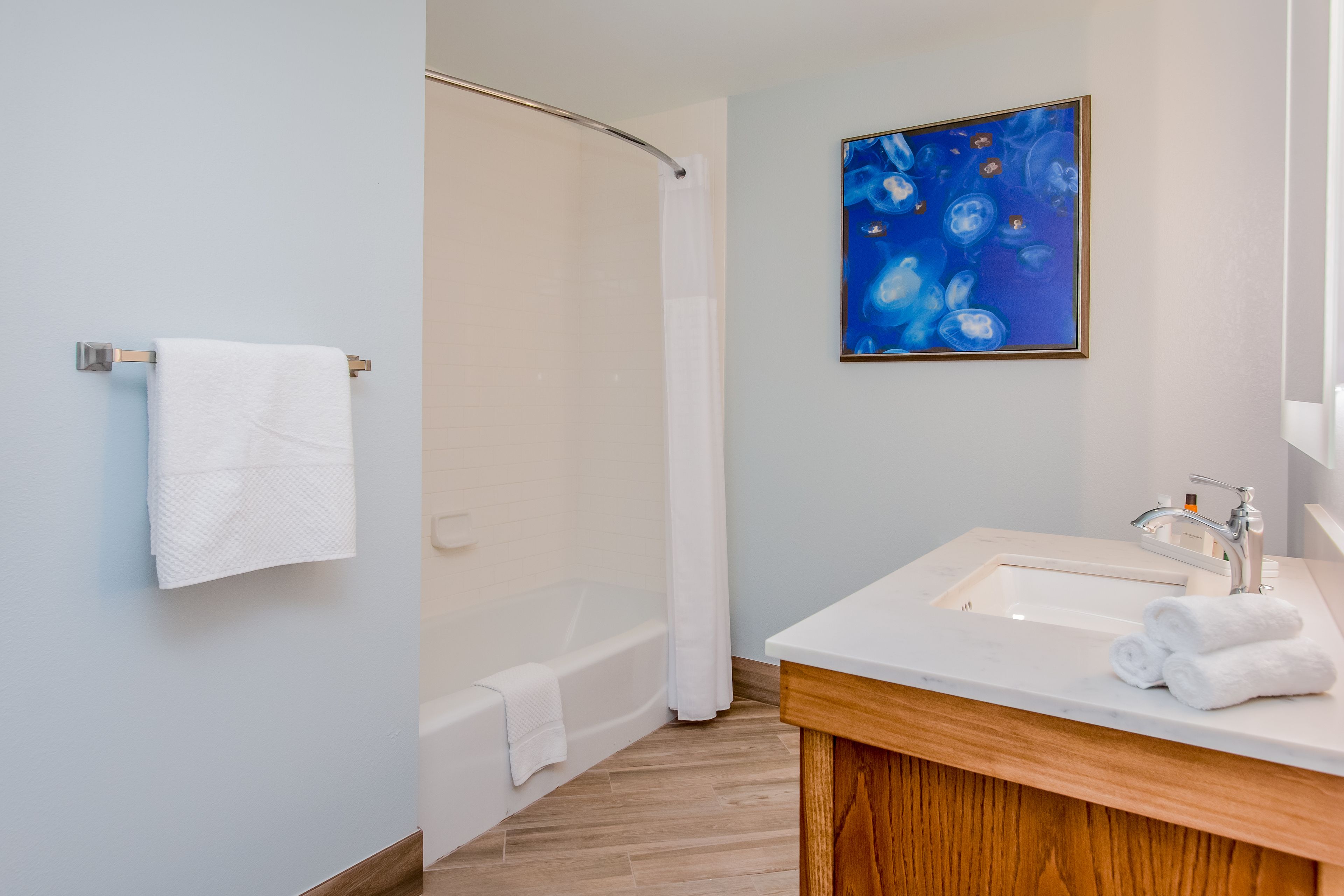 Un baño moderno con una bañera, un lavamanos con tocador de madera y un cuadro abstracto azul en la pared.