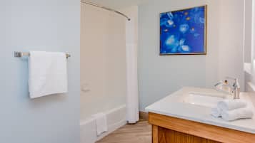 A modern bathroom with a bathtub, a sink with a wooden vanity, and a blue abstract painting on the wall.