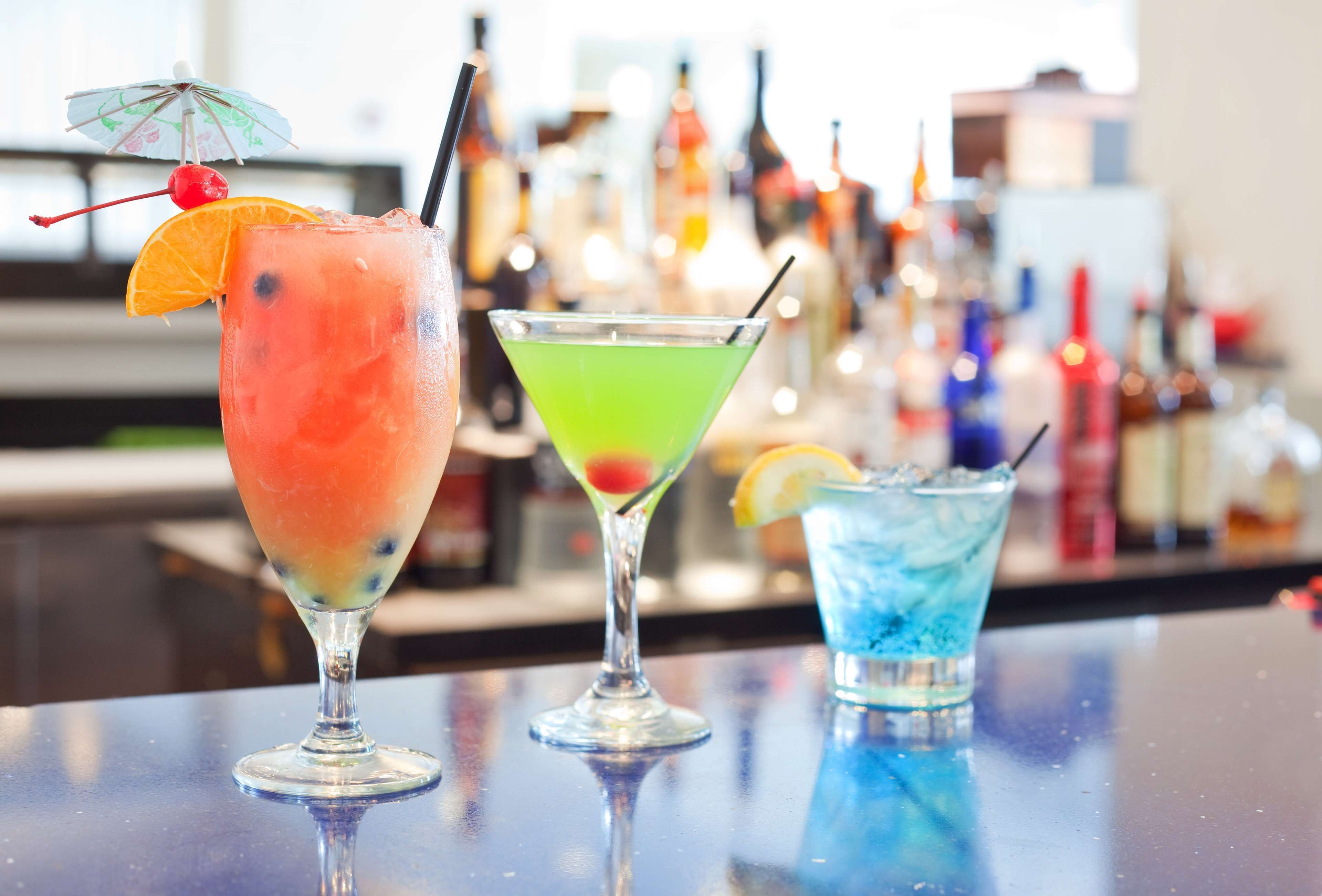 Three cocktails on a bar counter with a blurred background of various bottles.