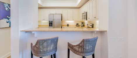 Eine moderne Küche mit weißen Schränken, einem Edelstahlkühlschrank und zwei Weidenbarhocker.