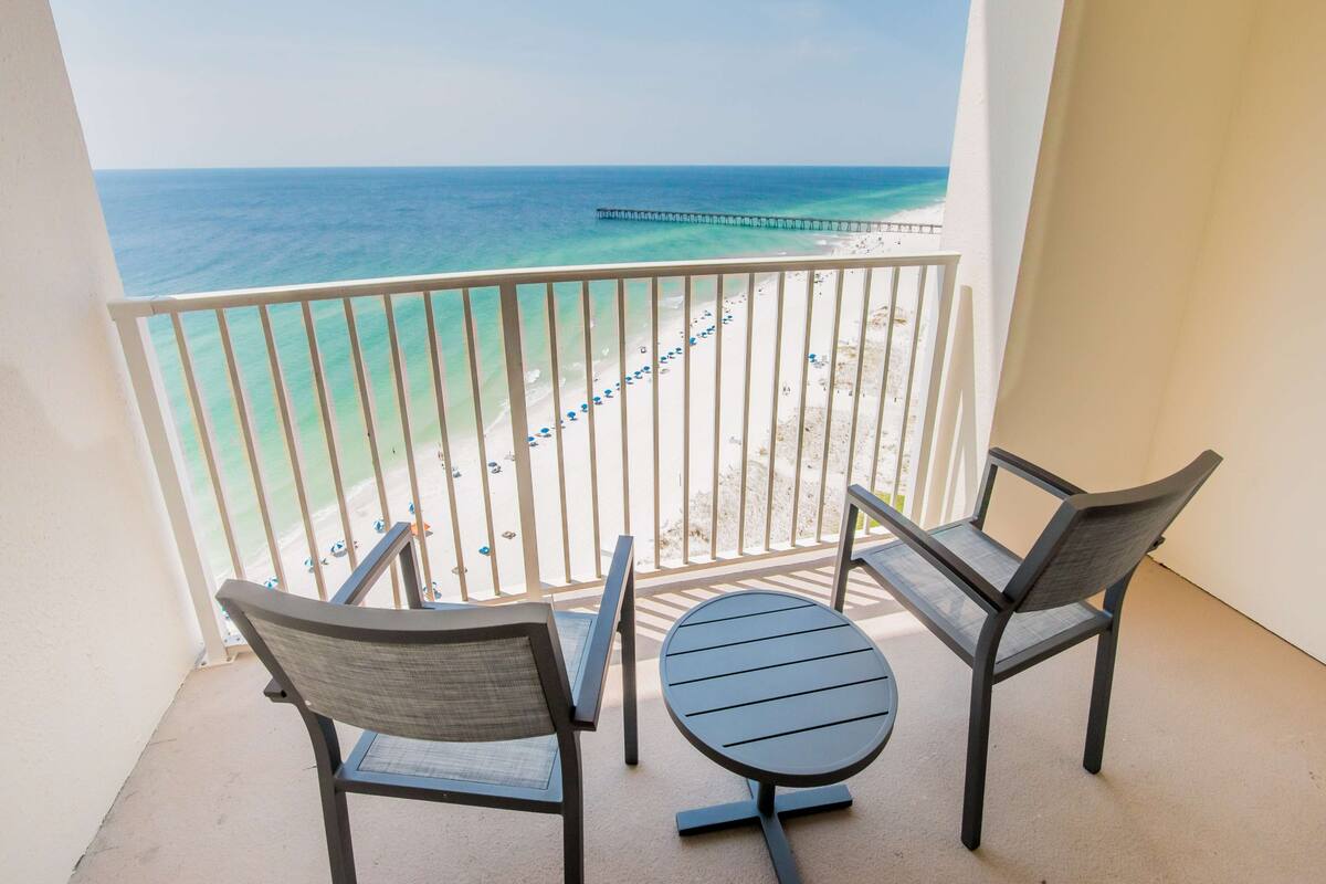 Un balcon avec deux chaises et une petite table, donnant sur une plage avec une jetée.