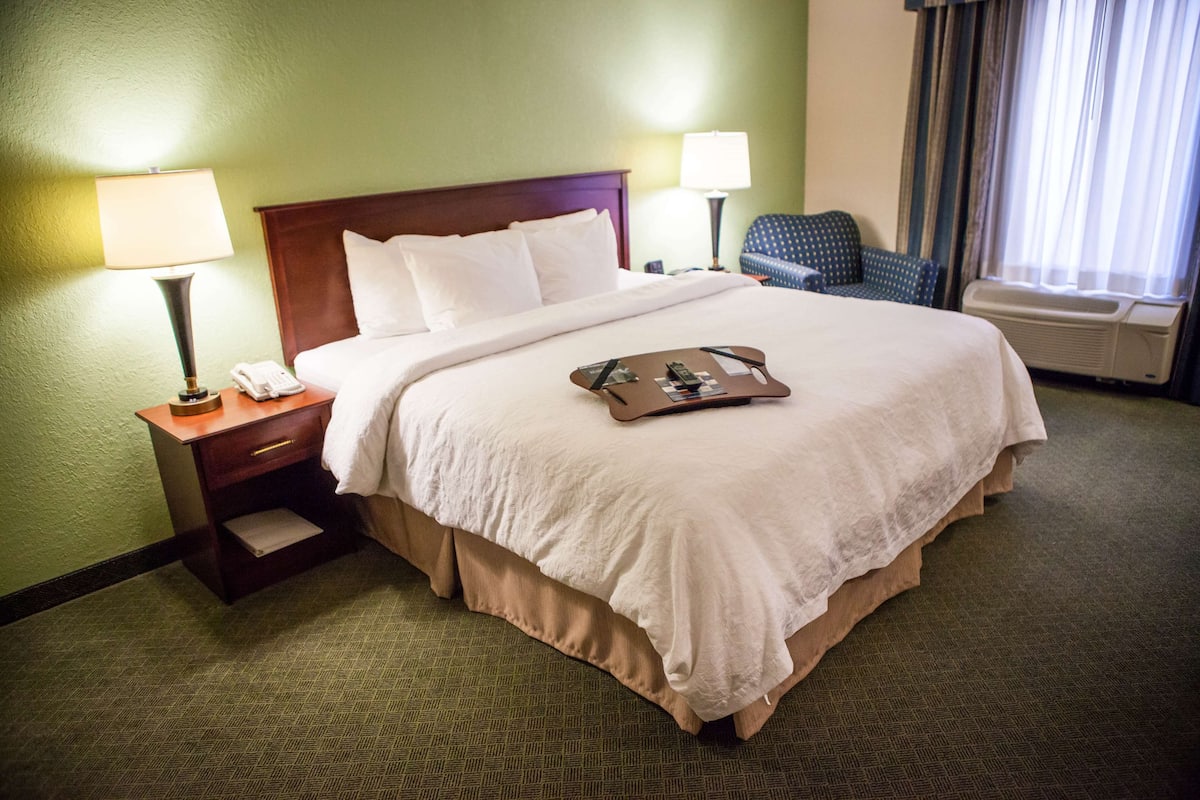 A hotel room with a large bed, two bedside tables with lamps, a chair, and a window with curtains.