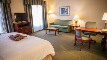A hotel room with a large bed, a sofa, a desk with a chair, a television on a stand, and two lamps.