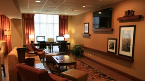 Quarto de hotel com área de estar, dois computadores, uma TV e quadros nas paredes.