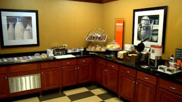 A hotel kitchen with wooden cabinets, a checkered floor, a coffee station, and framed pictures on the walls.