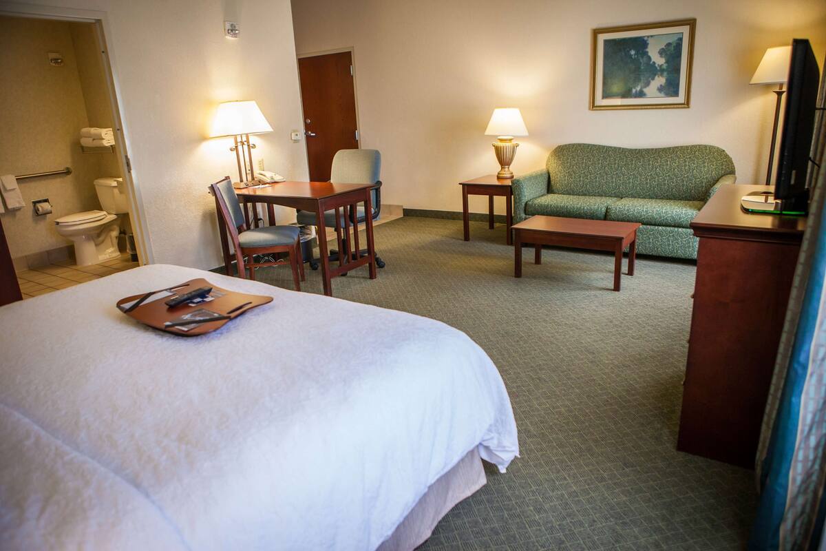 A hotel room with a bed, a desk, a chair, a sofa, and a TV.
