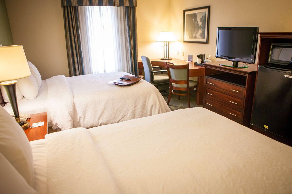 A hotel room with two beds, a desk with a computer, a television, and a refrigerator.