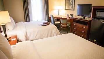 Una habitación de hotel con dos camas, un escritorio con ordenador, televisor y refrigerador.