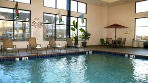 Piscina interior com espreguiçadeiras e mesa com guarda-sol.