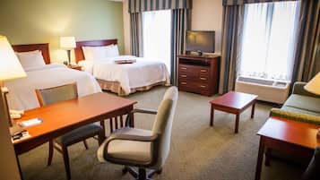 A hotel room with two beds, a desk, a chair, a television, and an air conditioning unit.