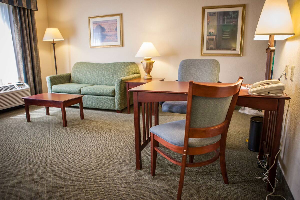 A hotel room with a green sofa, a wooden chair, a small table, a lamp, and a telephone.