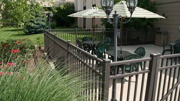 An outdoor patio with green chairs and a table, surrounded by a wooden fence and a lamp post.