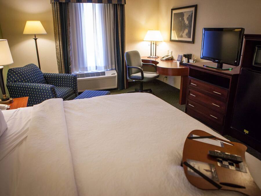 A hotel room with a large bed, a desk with a computer, a chair, a TV, and a minibar.