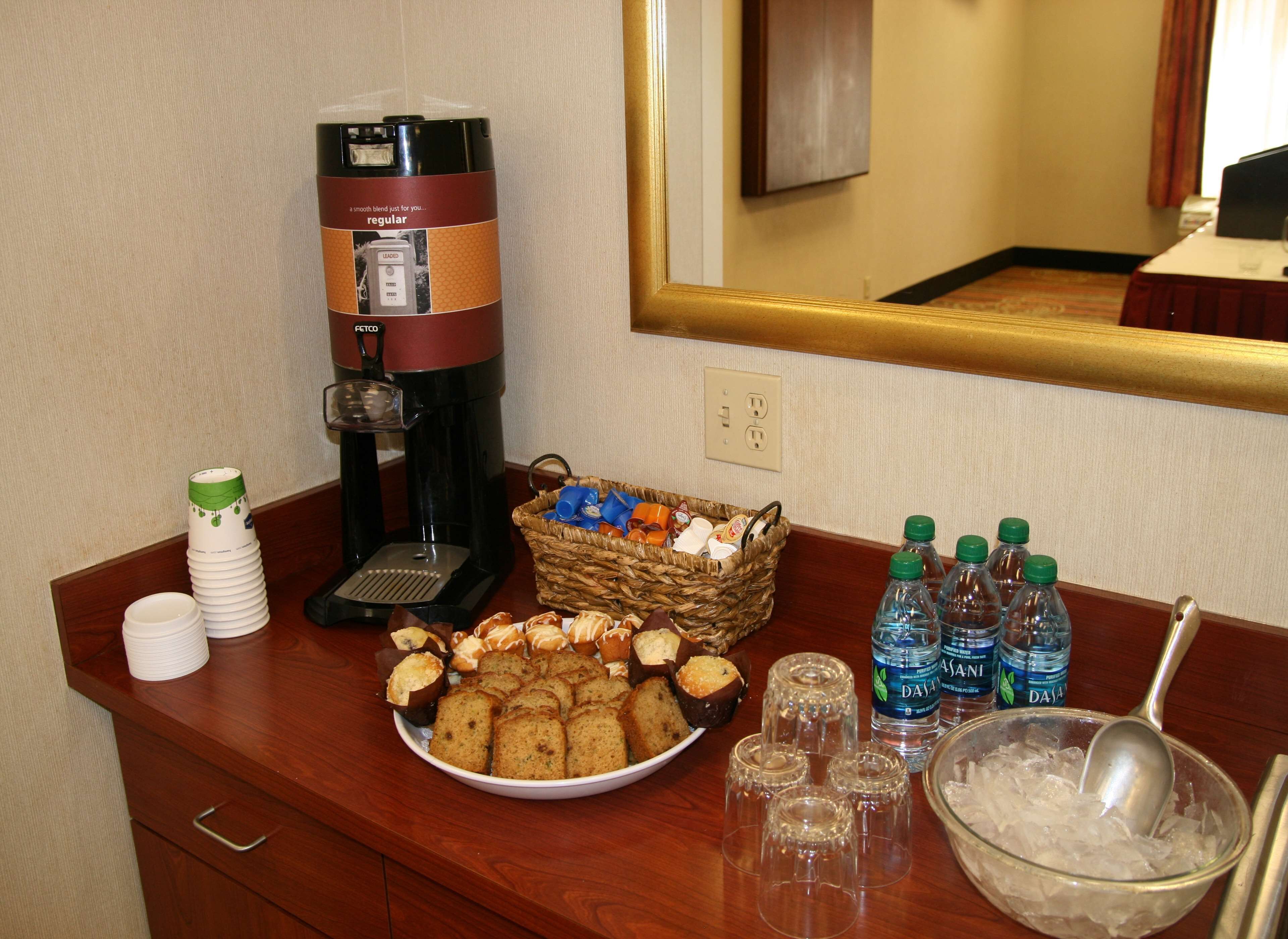 Un buffet avec une machine à café, un panier de muffins et des bouteilles d’eau.