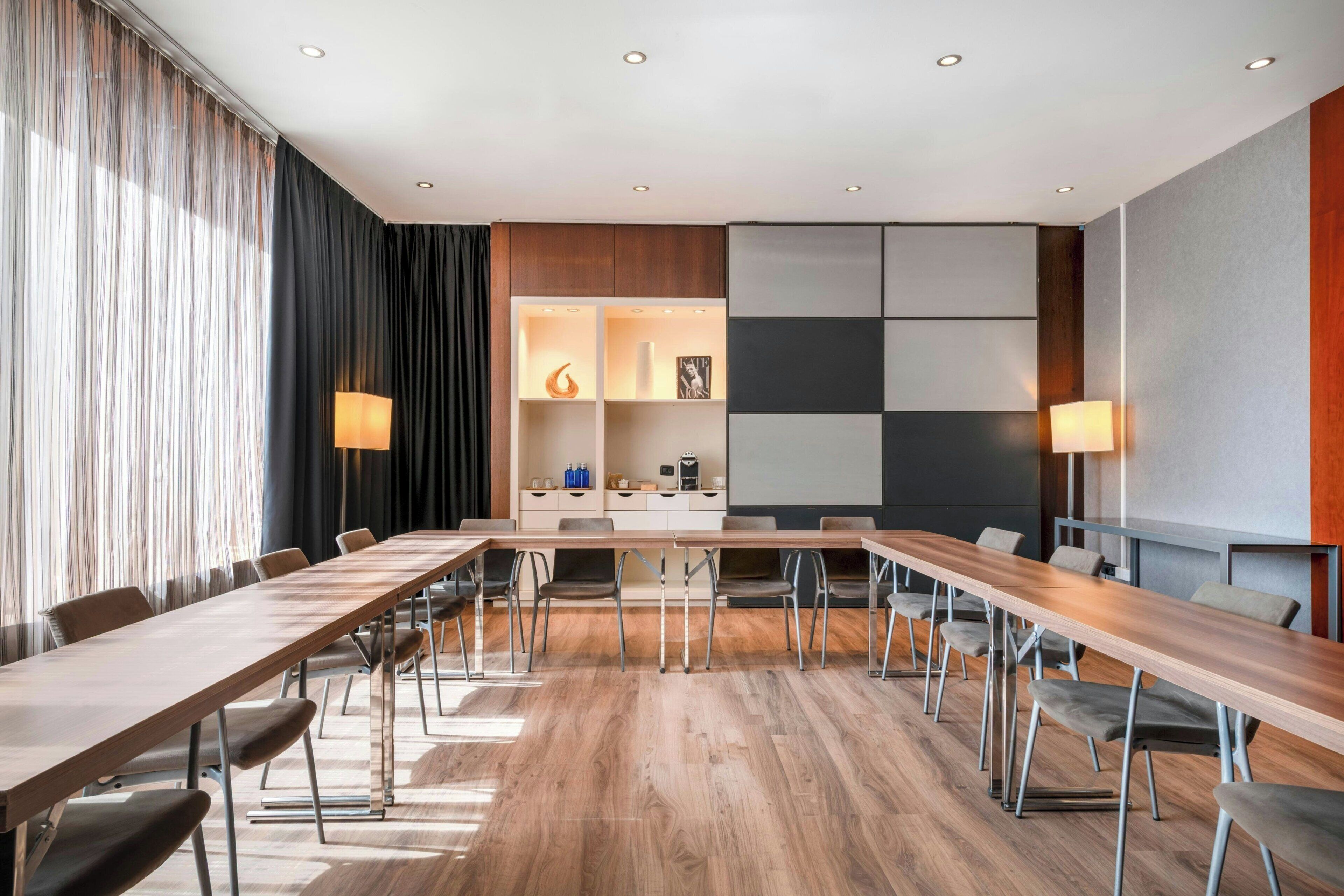 Een vergaderruimte met een lange tafel, stoelen, een projectiescherm en een muur met een geometrisch ontwerp.