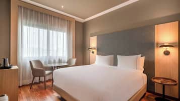 A hotel room with a large bed, a desk with a chair, a small round table, and a lamp.