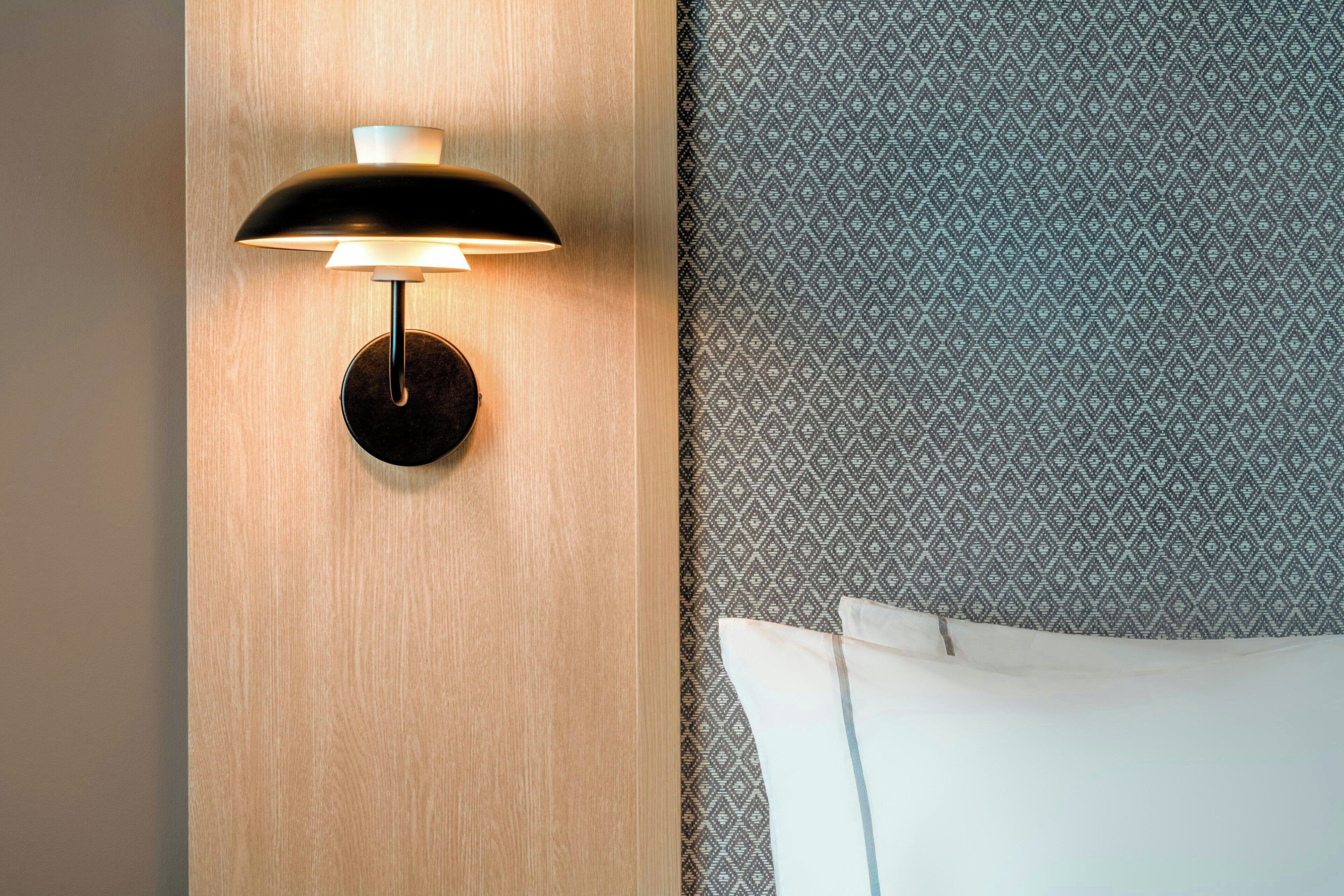 A wall-mounted light fixture with a round base, a wooden panel, and a patterned fabric backdrop.