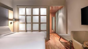 Una habitación de hotel con cama, una silla, escritorio y televisor en la pared.