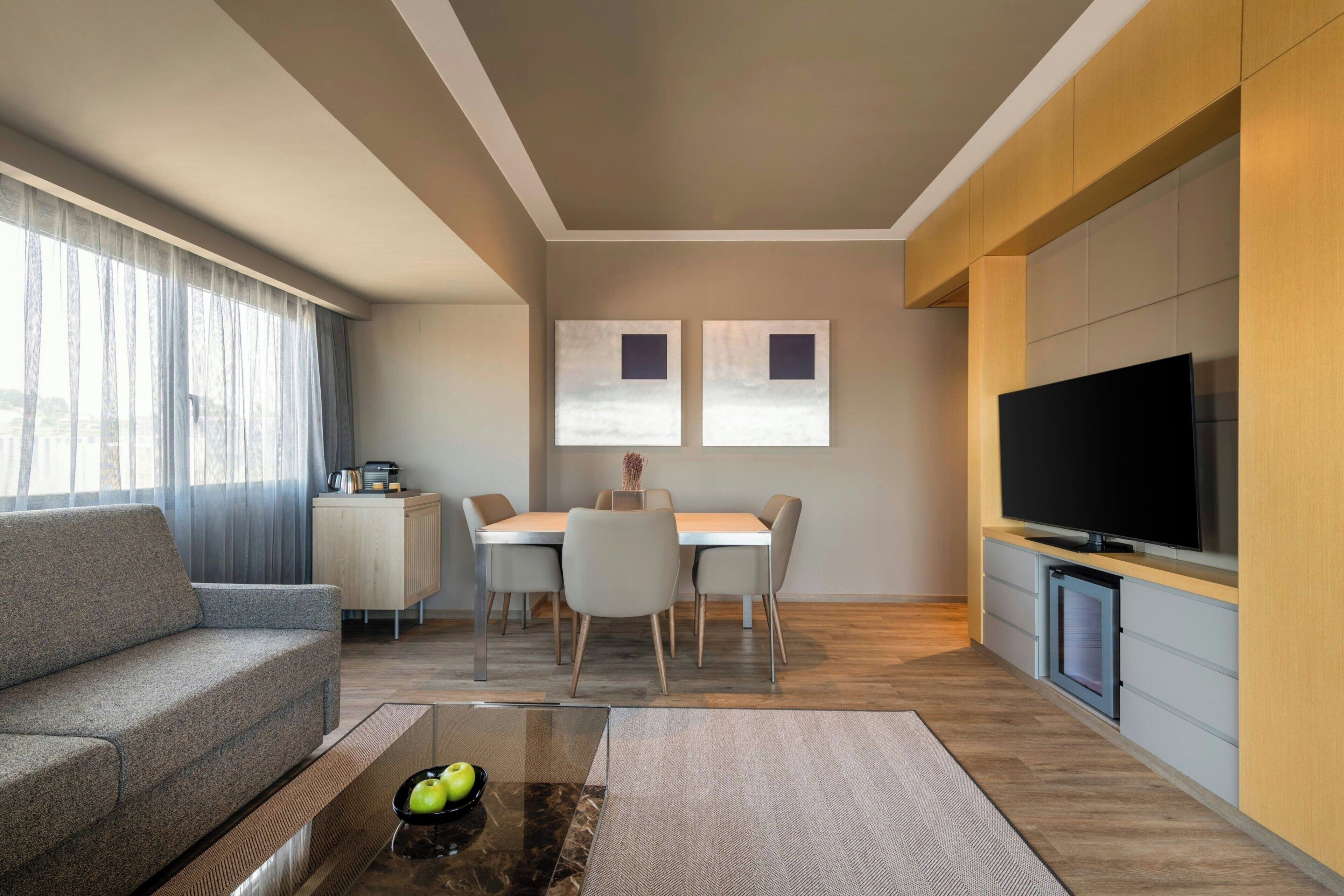 Una sala de estar moderna con sofá, mesa de centro, televisor, mesa de comedor, sillas y obras de arte en la pared.