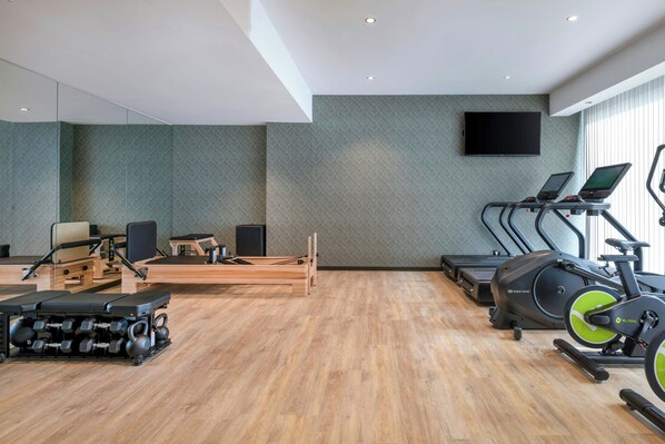 Un gimnasio moderno con equipo de ejercicio, un espejo grande y una televisión en la pared.