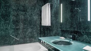 A modern bathroom with a glass sink, a white bathtub, and a large mirror.