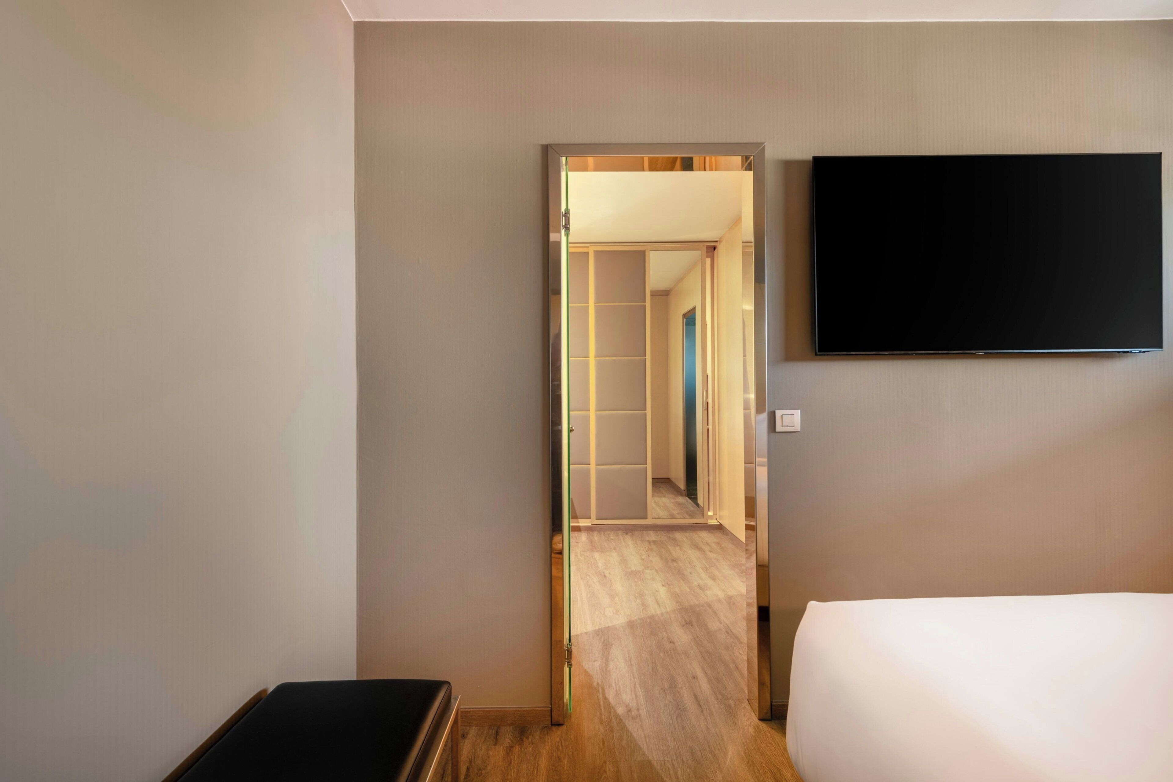 Habitación de hotel con cama, televisor de pantalla plana en la pared y piso de madera.