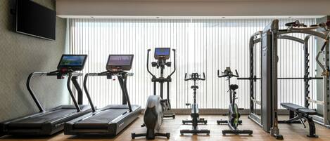 Un gimnasio con cintas de correr, bicicletas estáticas y una máquina de pesas.