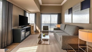 Una habitación de hotel moderna con televisión de pantalla plana, un sofá, una mesita de café y una lámpara.