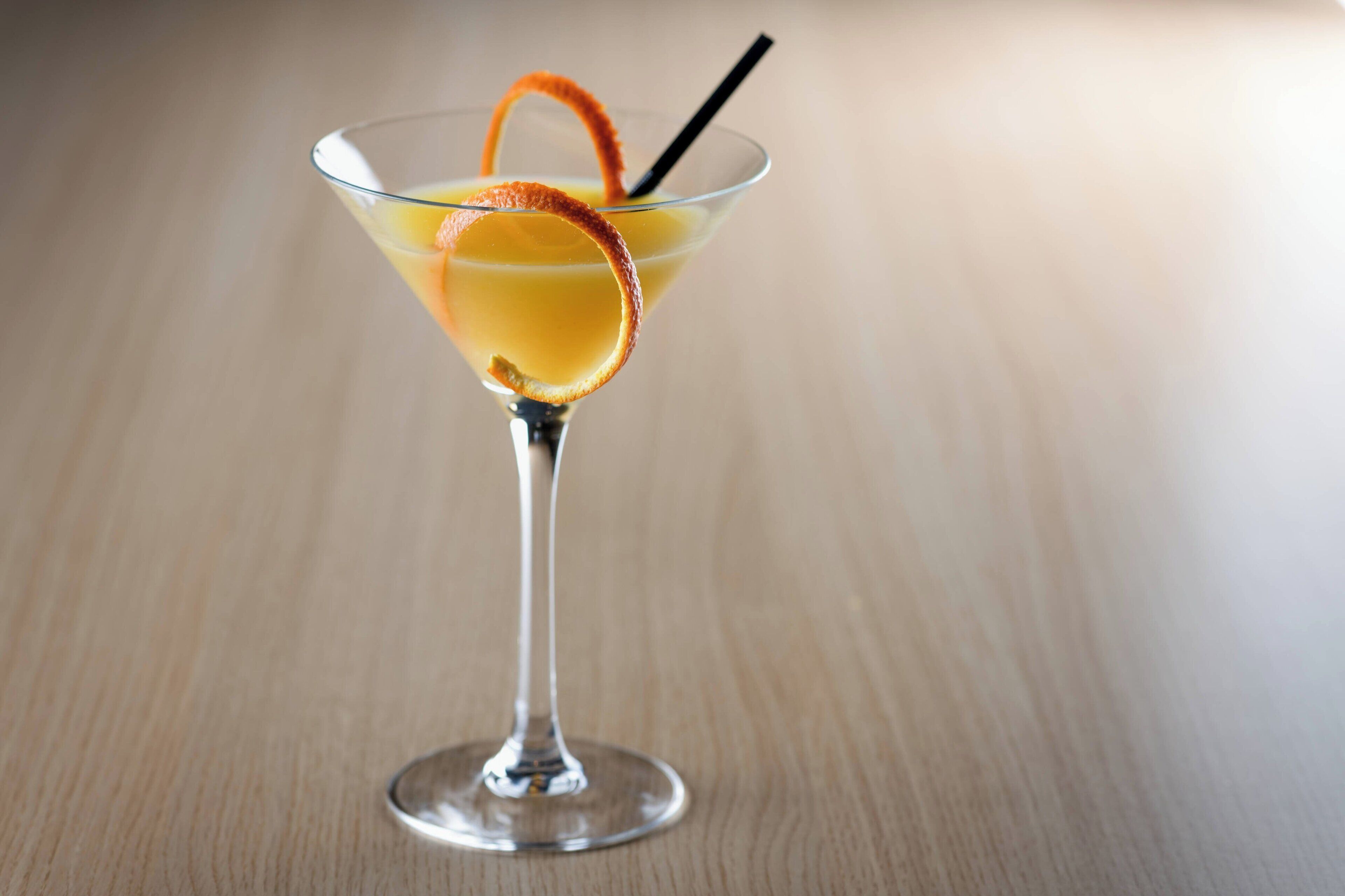 Un got de martini amb una pell de taronja com a guarnició i una canya sobre una superfície de fusta.