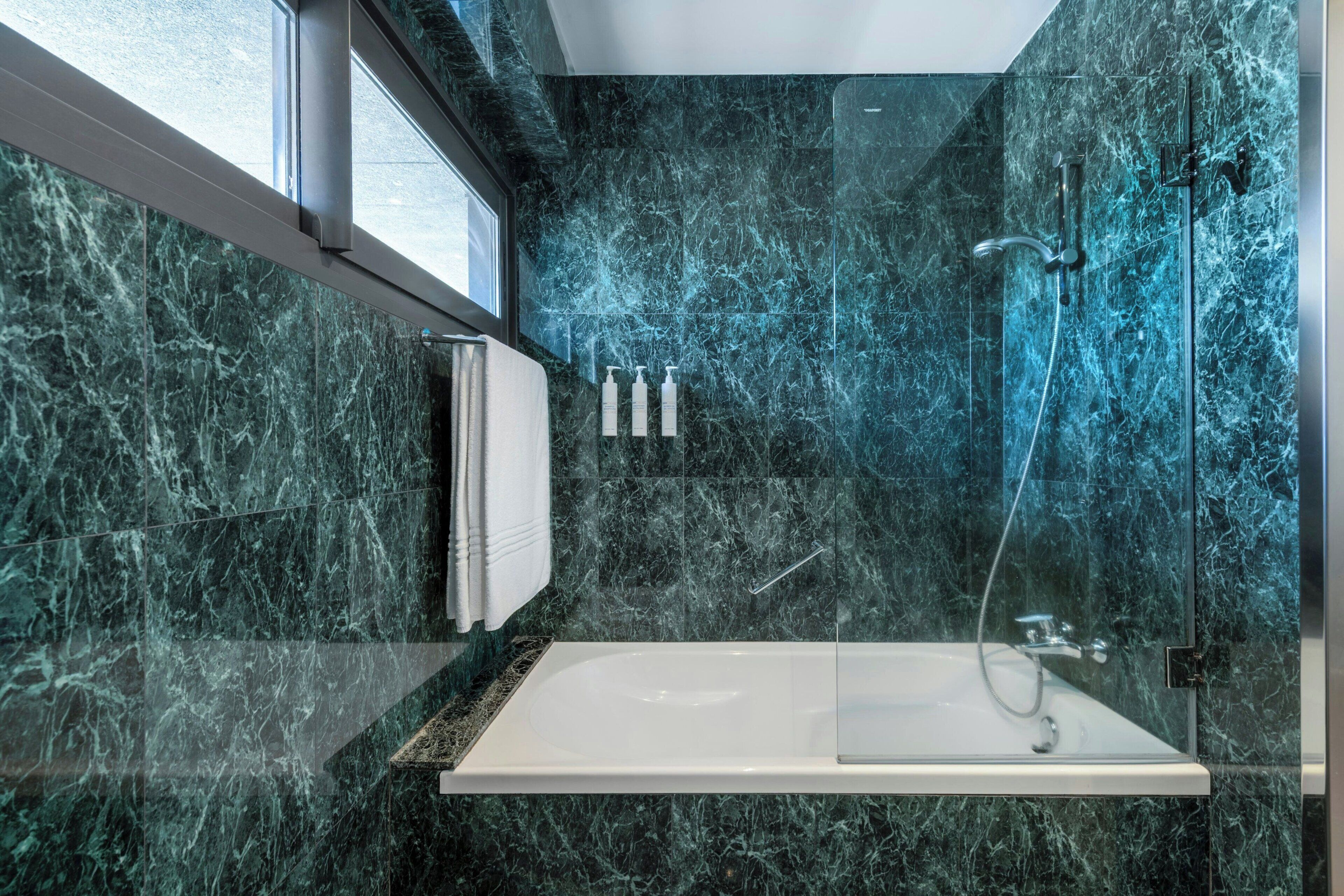 Un baño moderno con ducha envuelta en vidrio, una bañera blanca y un revestimiento de mármol.