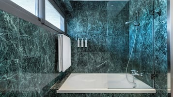 Un baño moderno con ducha envuelta en vidrio, una bañera blanca y un revestimiento de mármol.