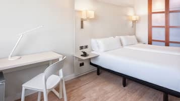 A hotel room with a bed, a desk, a chair, and two wall-mounted lamps.