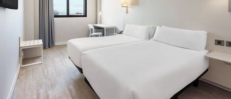 A hotel room with two beds, a desk, a chair, and a window with curtains.