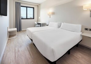 Une chambre d’hôtel avec deux lits, un bureau, une chaise et une fenêtre avec des rideaux.