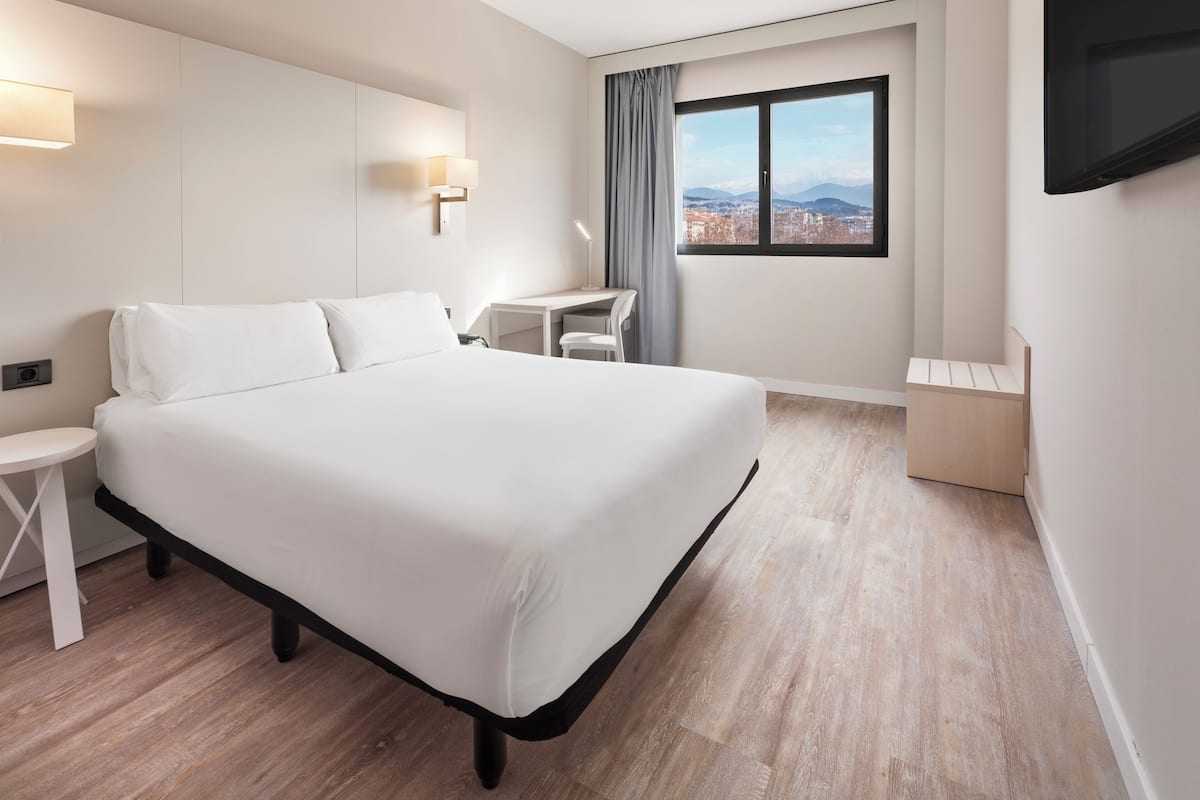 Et moderne hotelværelse med en stor seng, et skrivebord, en stol og et fjernsyn ophængt på væggen.
