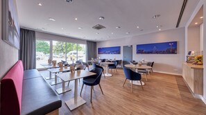 Ein moderner Essbereich mit Tischen, Stühlen, großen Fenstern und Kunstwerken an den Wänden.