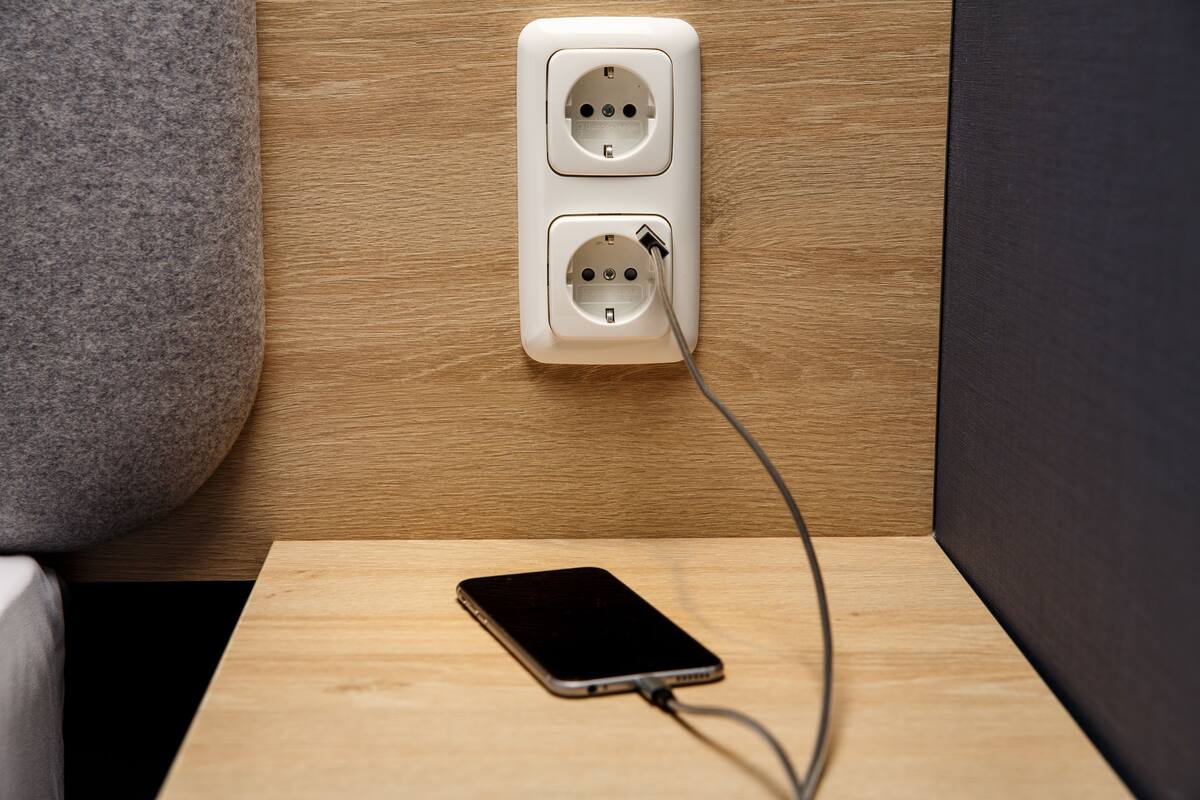 A smartphone charging on a wooden surface with a wall socket in the background.