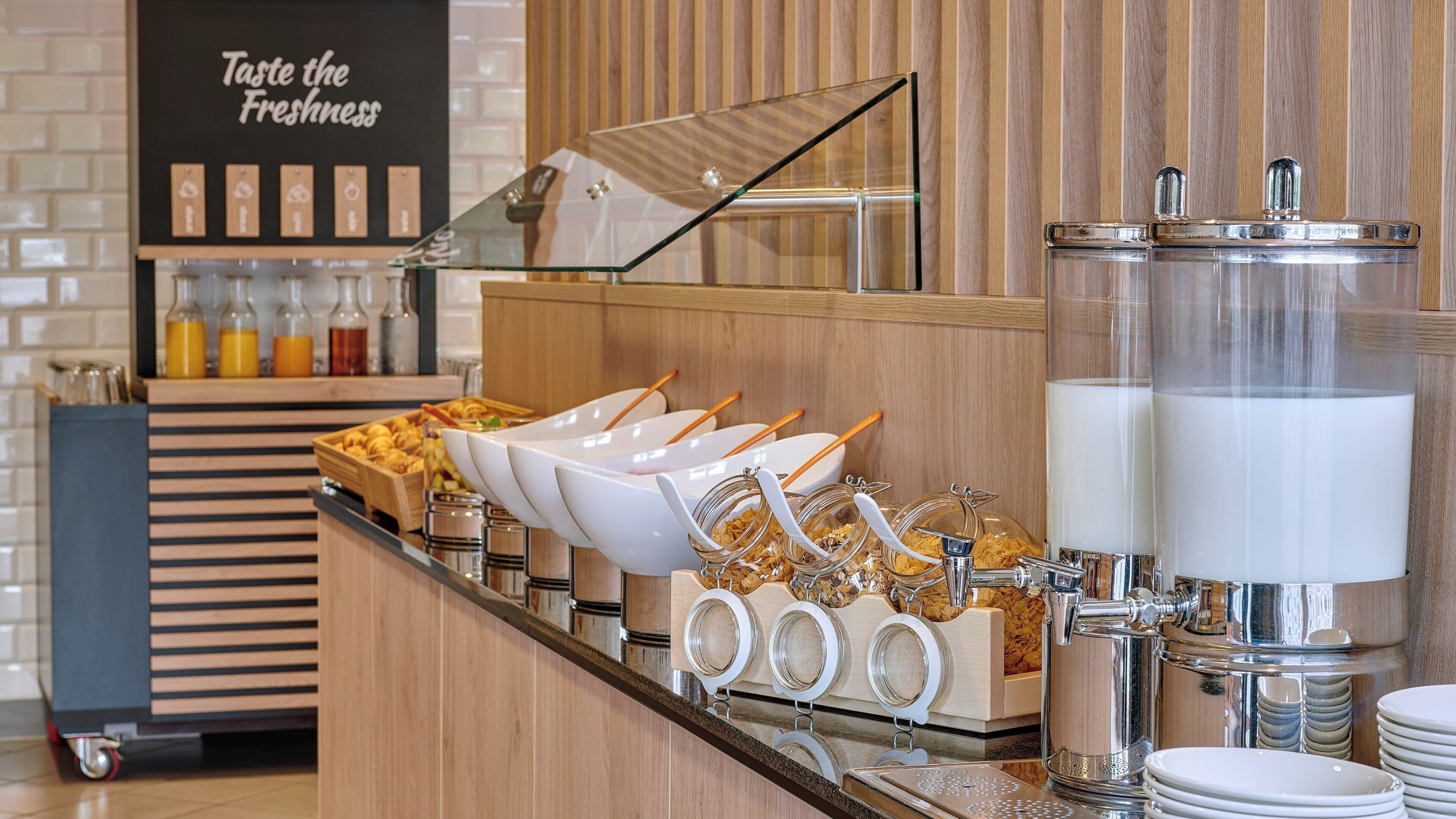 A buffet setup with various food items, serving utensils, and a milk dispenser.