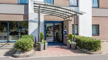 A hotel entrance with a covered walkway, glass doors, and potted plants.