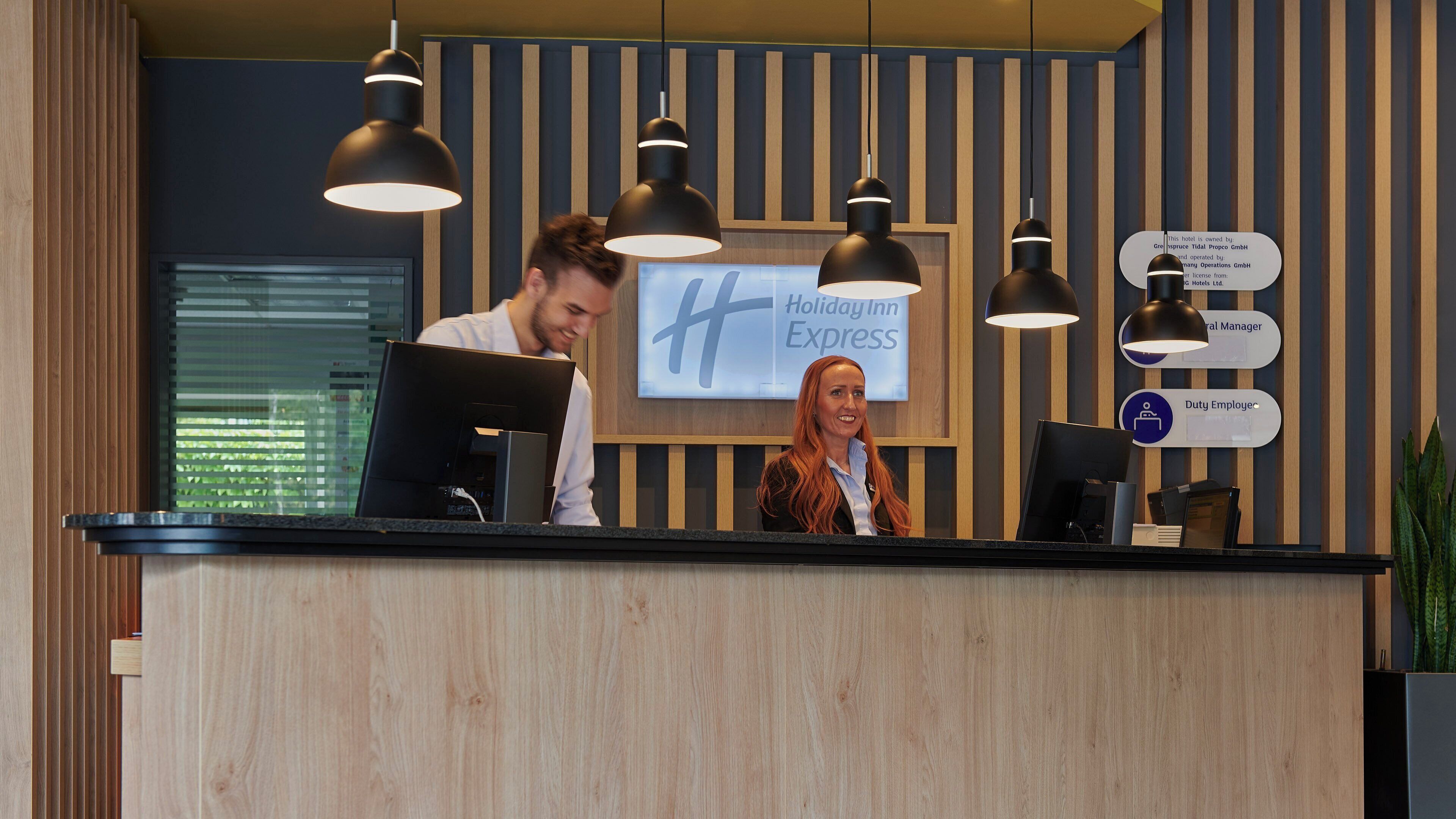 A hotel reception desk with a sign for Holiday Inn Express, a computer, and a plant.