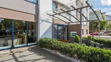 A hotel entrance with a glass canopy, a sign for Holiday Inn Express, and a paved walkway with greenery.