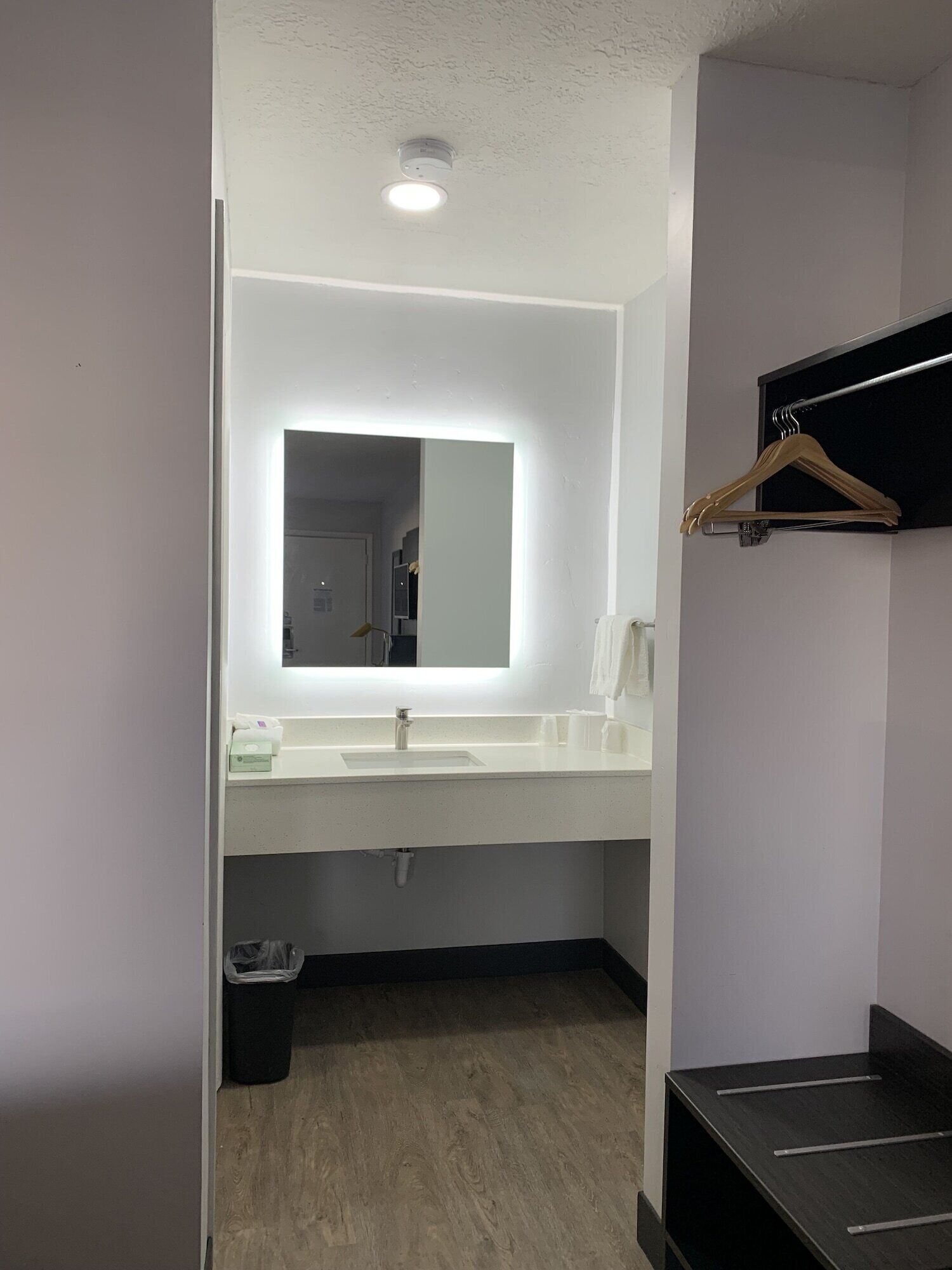 Un baño moderno con un espejo grande, encimera blanca y repisa negra con un perchero de madera.