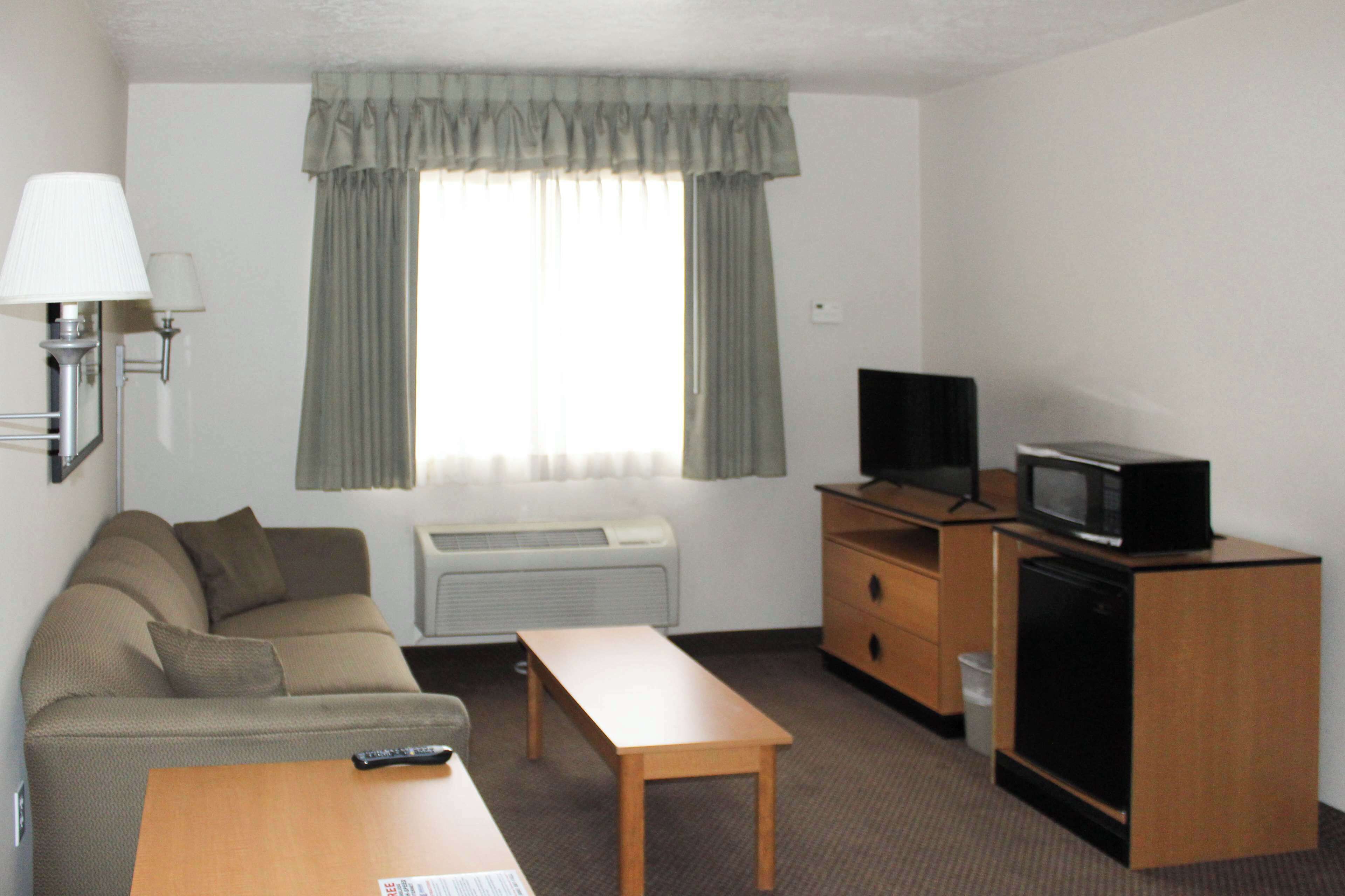 A compact hotel room with a sofa, a small wooden table, a television on a wooden cabinet, and a window with curtains.