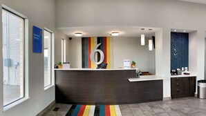 A modern reception area with a dark reception desk, a colorful striped rug, and a large '6' sign on the wall. - Motel 6 Ogden, UT - 21st Street (Ogden)