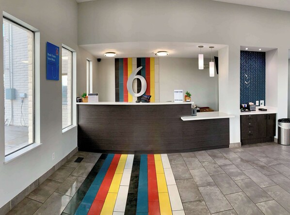 Un espace d’accueil moderne avec un comptoir d’accueil foncé, un tapis rayé aux couleurs vives et un grand panneau représentant le chiffre « 6 » sur le mur.