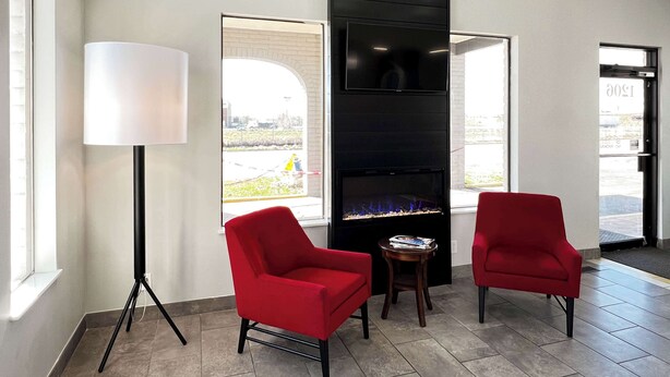 A modern lobby with two red chairs, a floor lamp, a fireplace, and large windows offering a view of the outside. - Motel 6 Ogden, UT - 21st Street (Ogden)