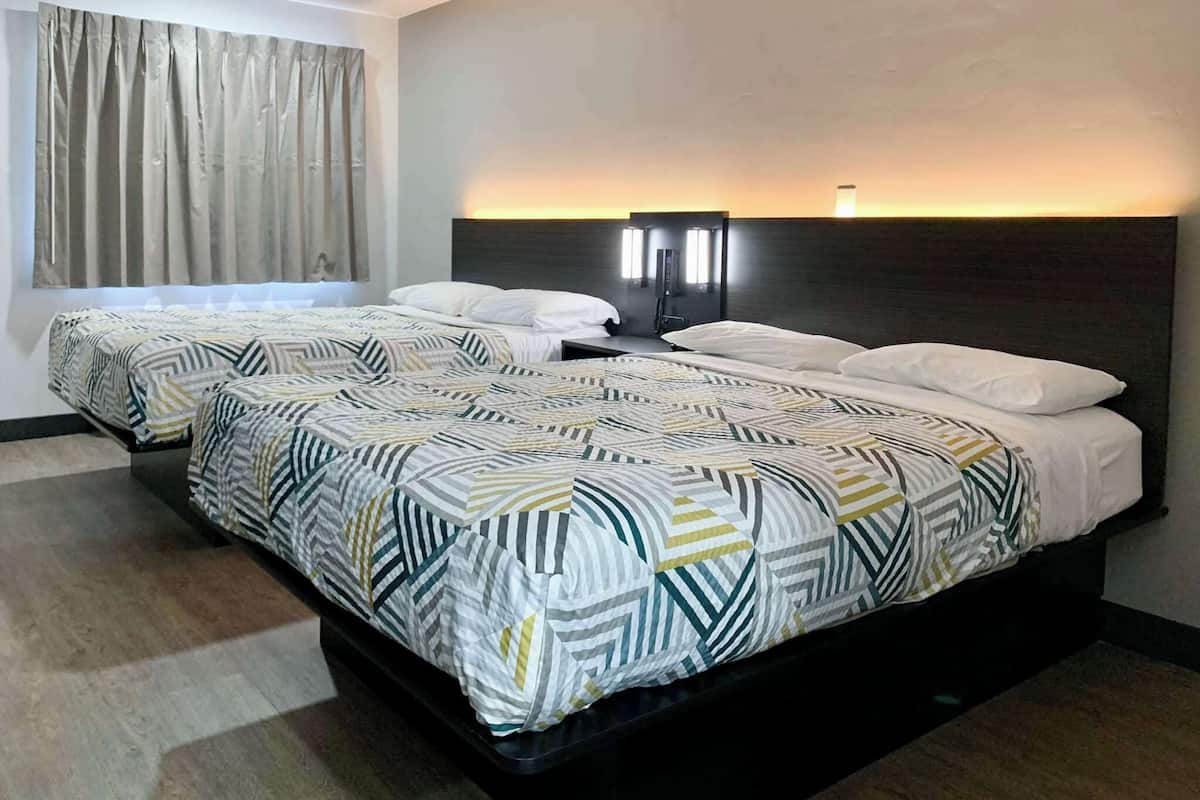 A hotel room with two beds, each with patterned bedding, a headboard with built-in lighting, and a window with curtains.